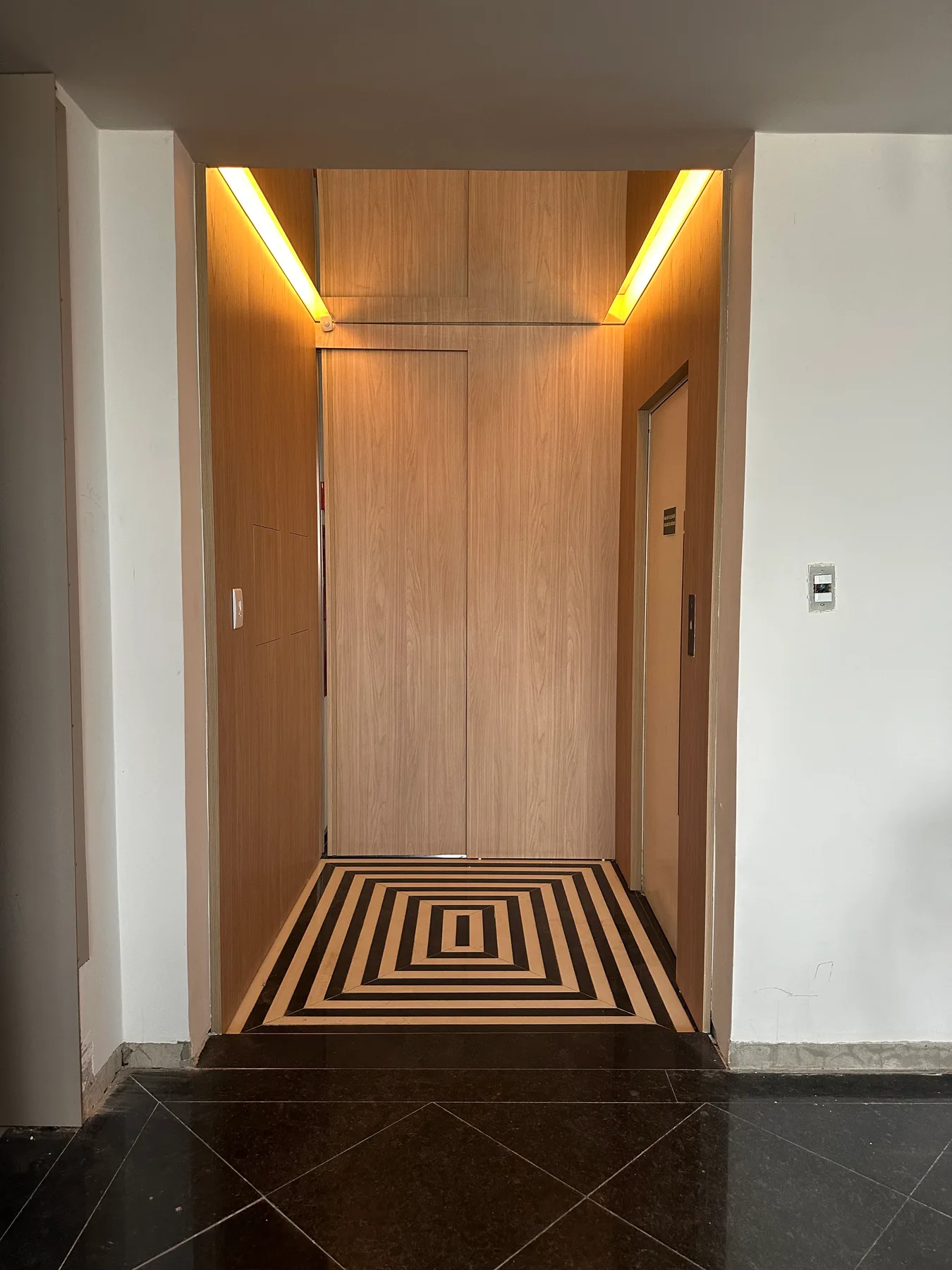 Hall de elevador com piso em pedra e paginação geométrica