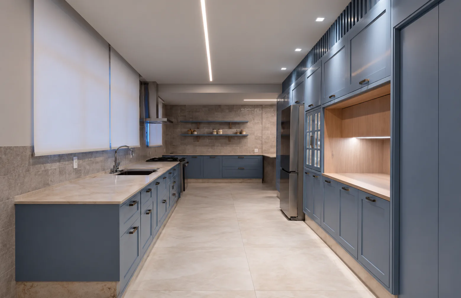 Cozinha com bancada em pedra clara, marcenaria azul e iluminação embutida